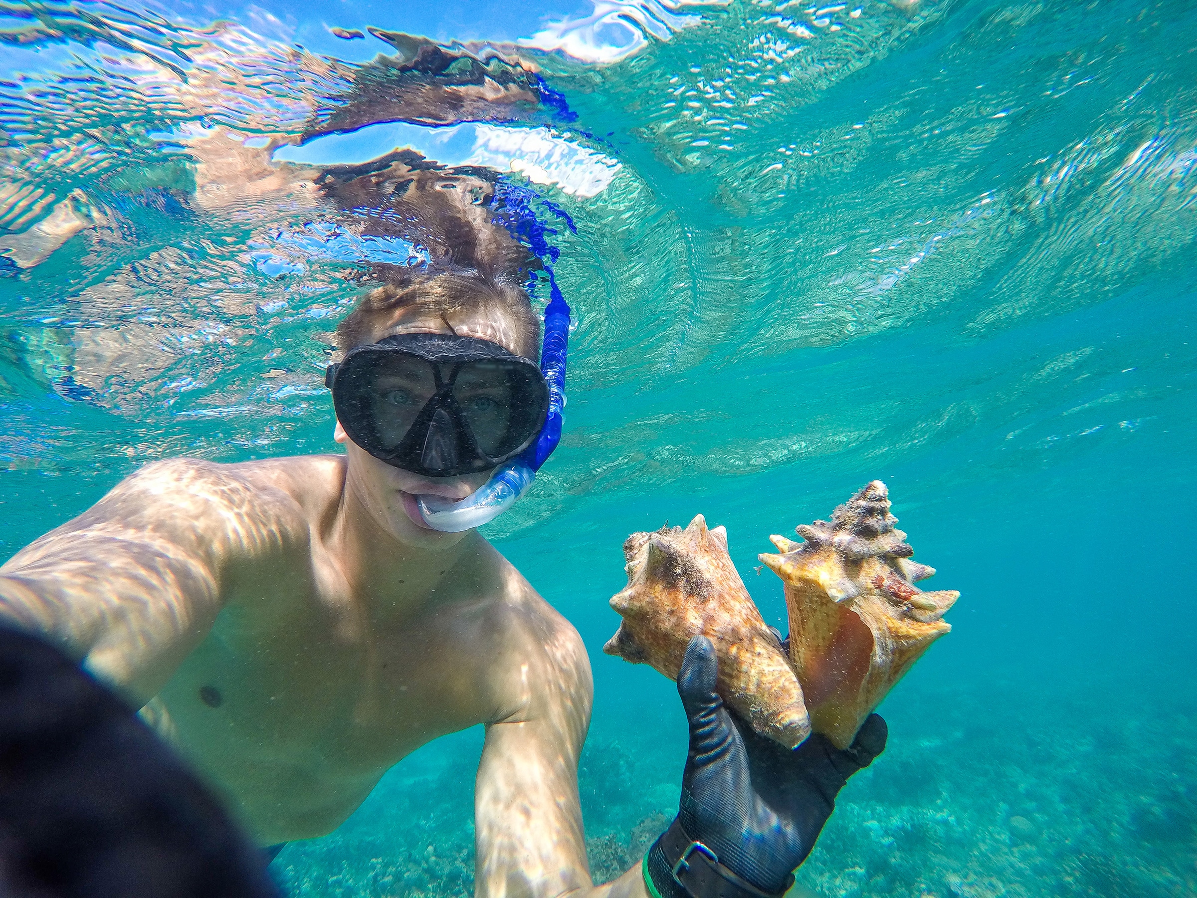 Underwater wide angle selfie of muscular freediver with two shell